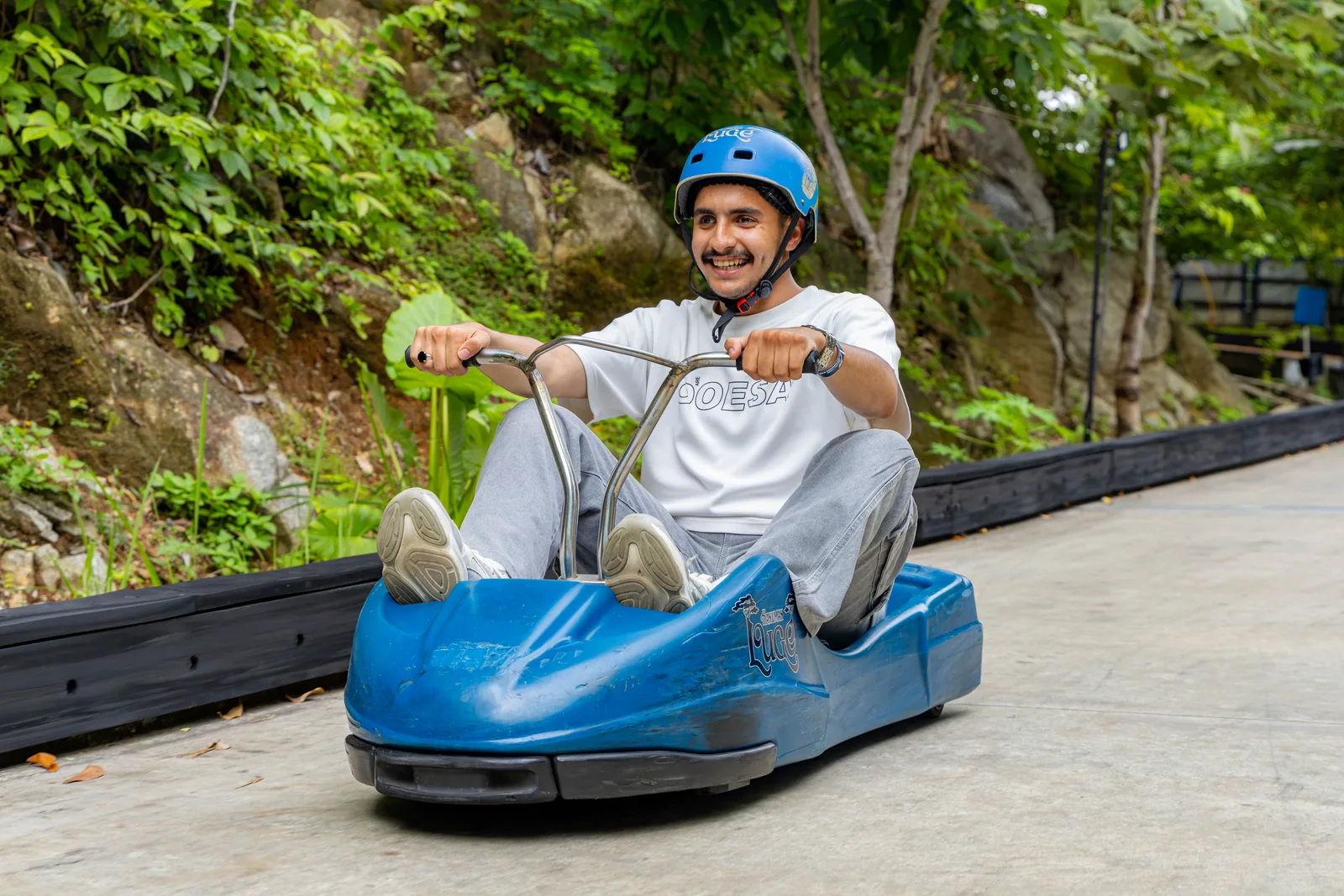 An adult rider wearing a blue helmet with both hands on the luge handlebars.
