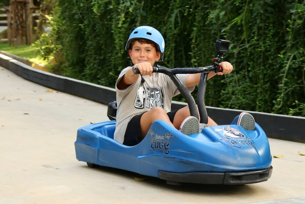 A young helmeted rider holding the handlebars of a blue luge cart.