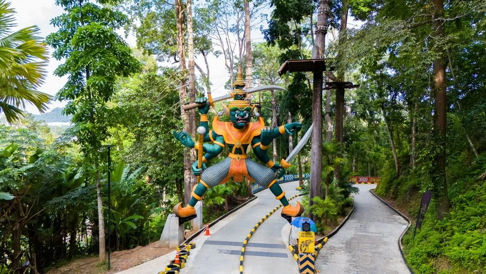 A large colourful guardian figure beside the luge track among trees.